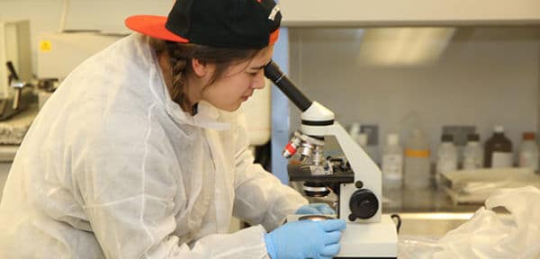 Young native woman looks into a microscope. She is wearing a protective cover over her clothes and hands.