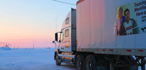 A semi truck in a snowy area with the sun setting.